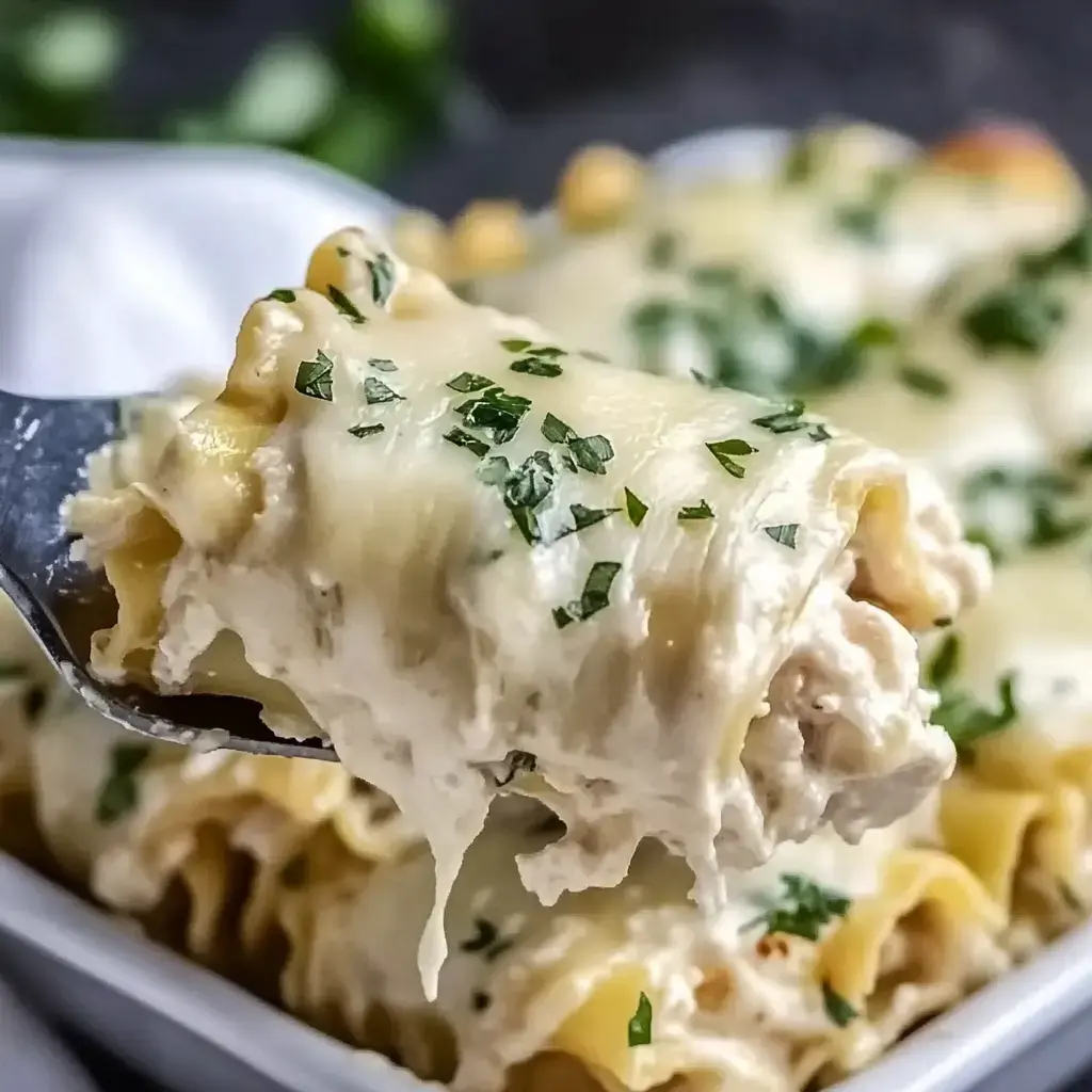 Une fourchette portant un plat crémeux de pâtes au poulet garnies de persil, avec d'autres portions visibles en arrière-plan.