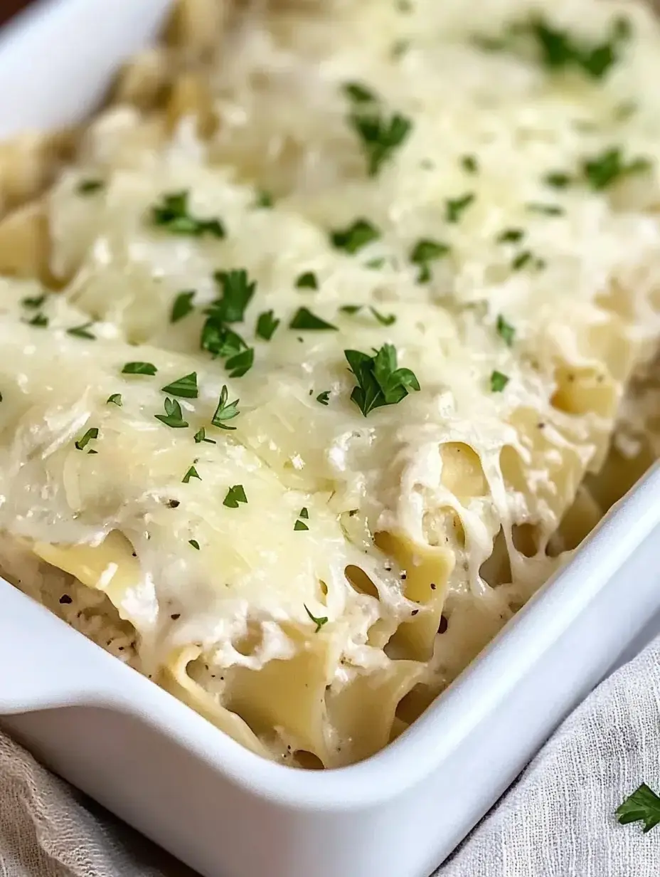 Gros plan sur un plat de pâtes crémeuses recouvert de fromage fondu et garni de persil haché, servi dans un plat de cuisson blanc.