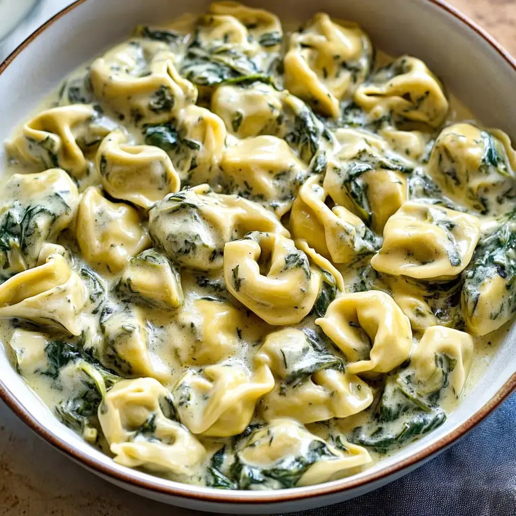 Un bol de tortellini avec une sauce crémeuse et des épinards.