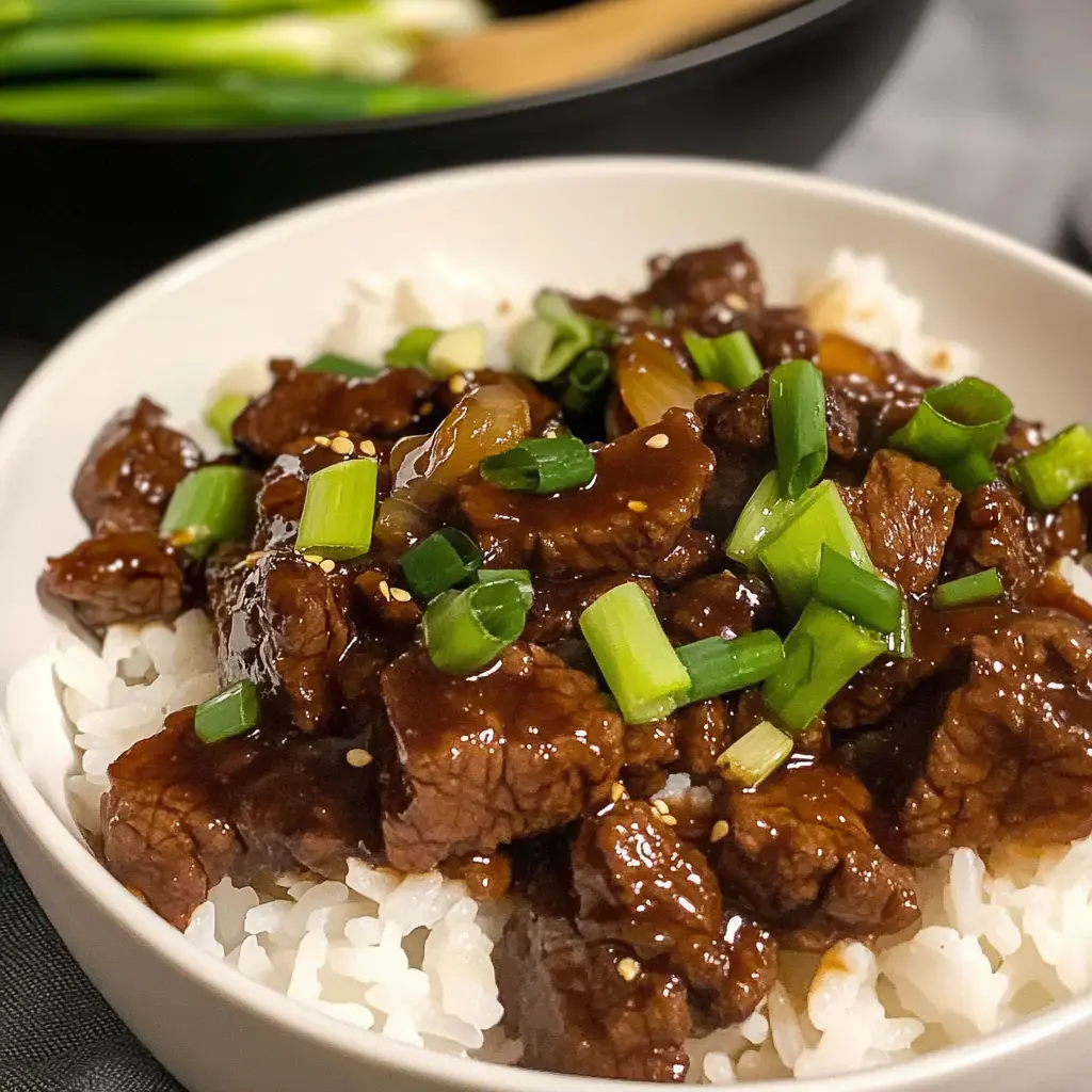 Un bol de riz blanc garni de morceaux tendres de bœuf dans une sauce brune et décoré de ciboule.