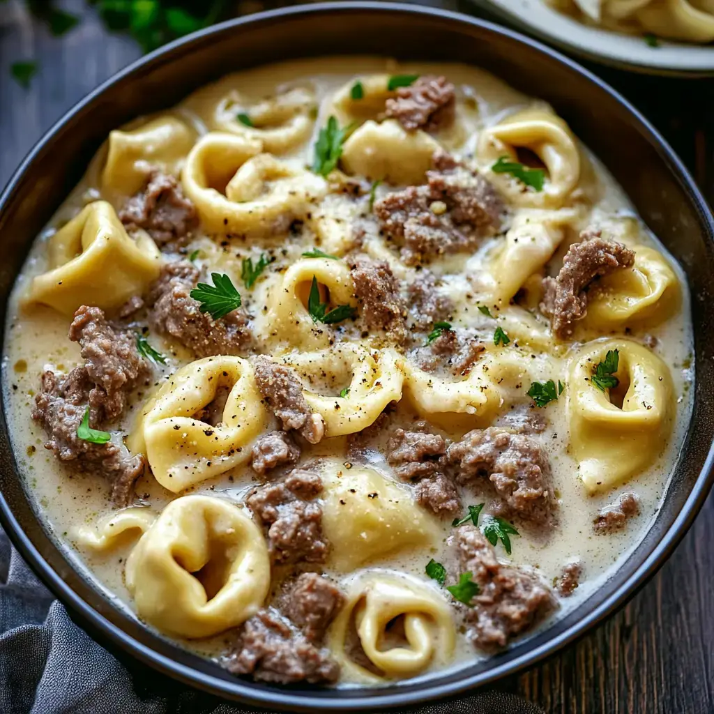 Un bol rempli de tortellinis crémeux avec du steak et garni de persil et poivre noir en gros plan.