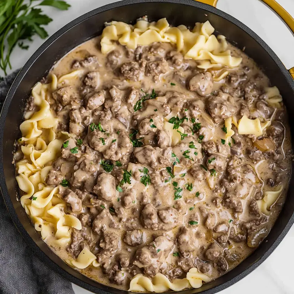 Un gros plan d'une poêle remplie de bœuf stroganov crémeux servi sur des nouilles aux œufs et décoré de persil haché.