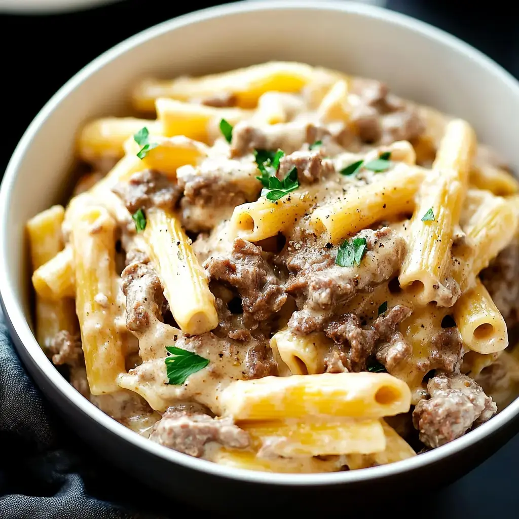 Un bol de pâtes crémeuses, avec des rigatoni mélangés à du bœuf haché et garnis de persil.