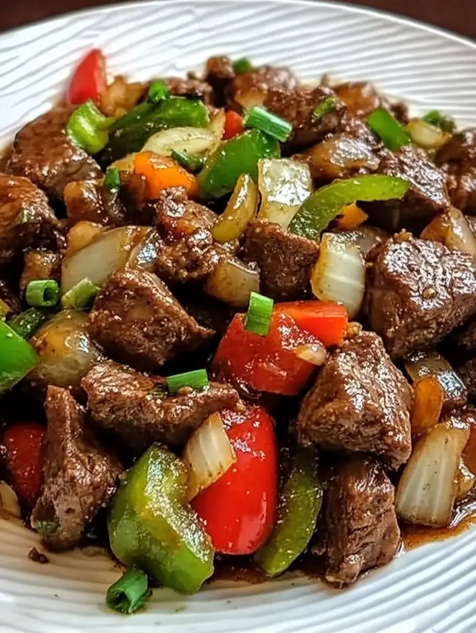 Un gros plan d'une assiette de morceaux de bœuf sautés avec des poivrons colorés, des oignons et des oignons verts dans une sauce savoureuse.