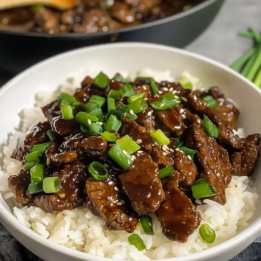 Un bol de riz blanc surmonté de bœuf sauté et garni d'oignons verts hachés et de graines de sésame.
