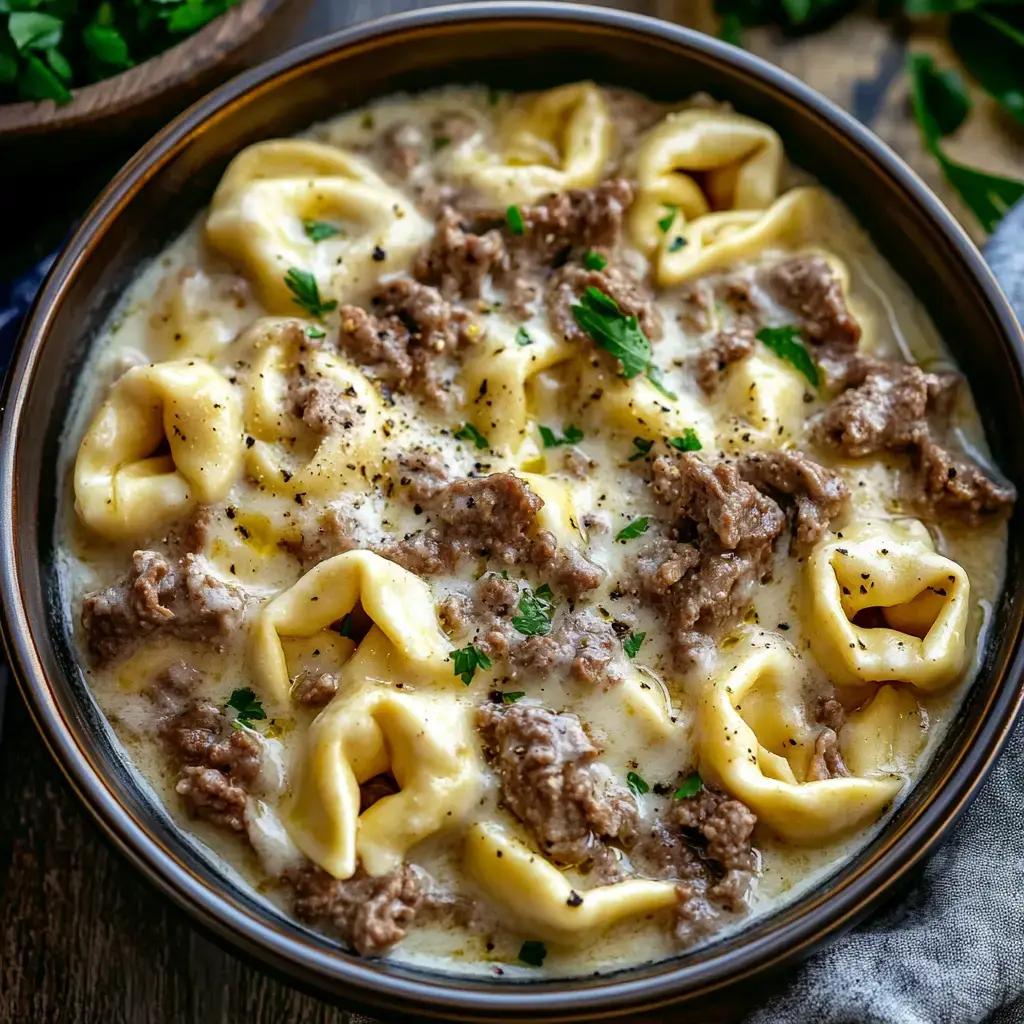 Un bol de soupe crémeuse aux tortellini avec du bœuf haché et garni de persil frais.