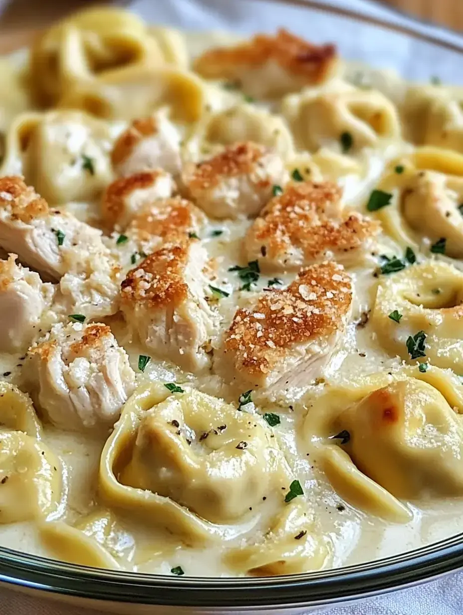 Un plat de pâtes crémeux avec des morceaux de poulet dorés et des tortellini farcis au fromage, garni de persil.