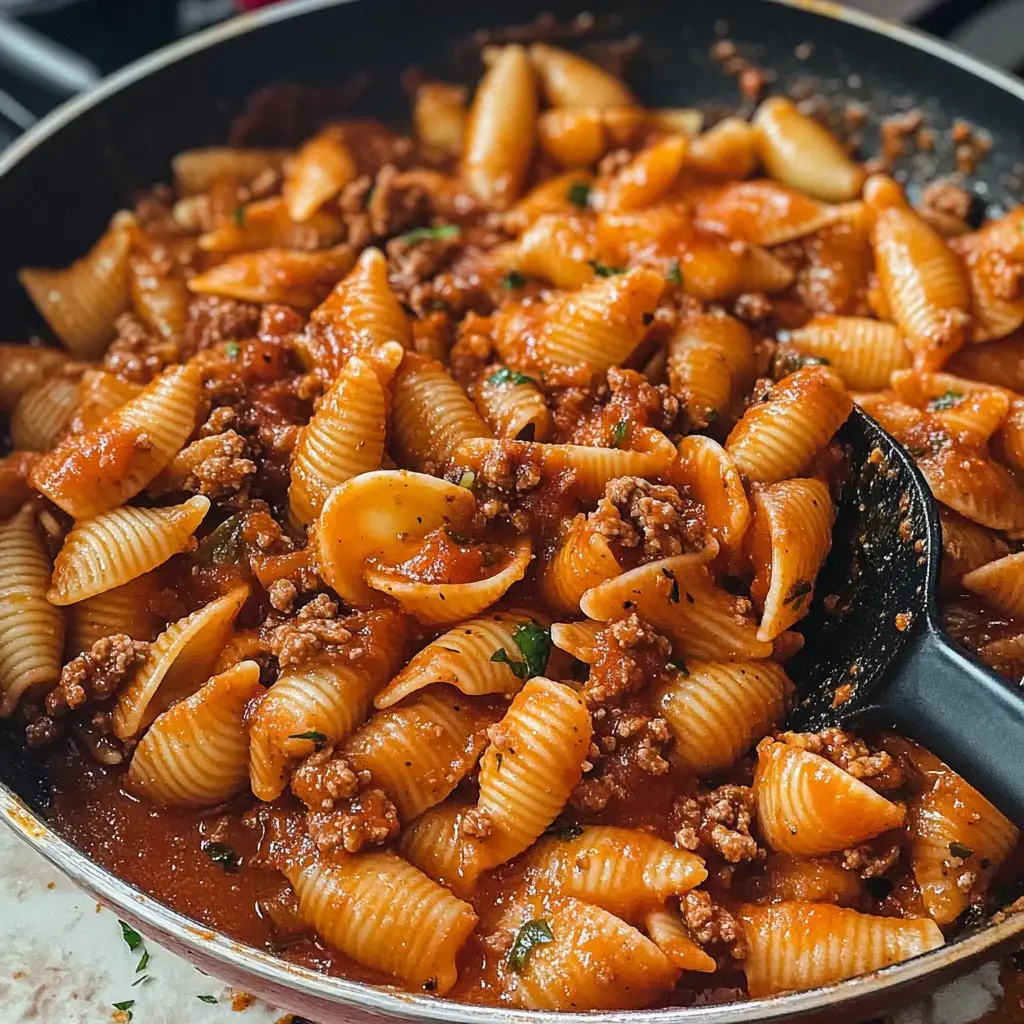 Une vue rapprochée d'une poêle remplie de coquillages de pâtes mélangés à de la viande hachée dans une sauce tomate.