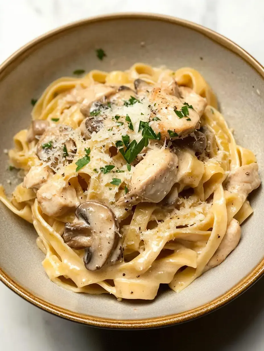 Un bol de pâtes tagliatelles crémeuses garnies de poulet sauté, de champignons, de fromage râpé et de persil.