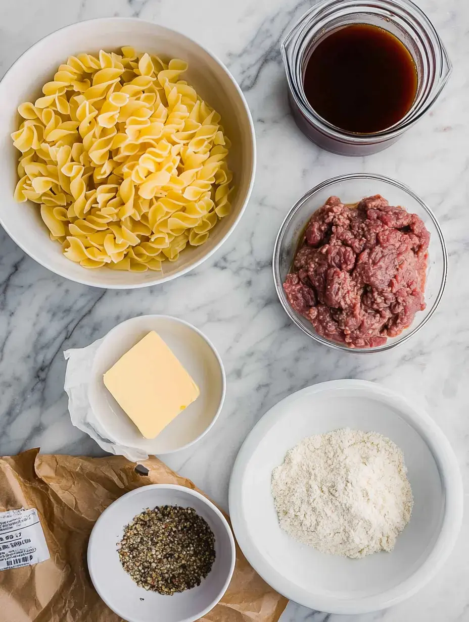 Vue d'ensemble des ingrédients pour une recette, incluant des pâtes farfalle, du bœuf haché, du beurre, de la farine, du bouillon et un mélange d'épices, disposés sur un plan de travail en marbre.