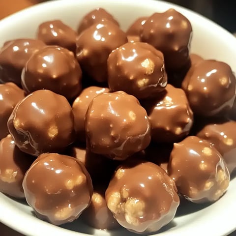 Zoom sur des boules brillantes enrobées de chocolat empilées dans un bol blanc.