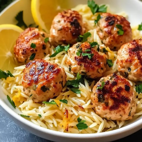 Un bol d'orzo accompagné de boulettes dorées, parsemé de persil frais et de quartiers de citron.